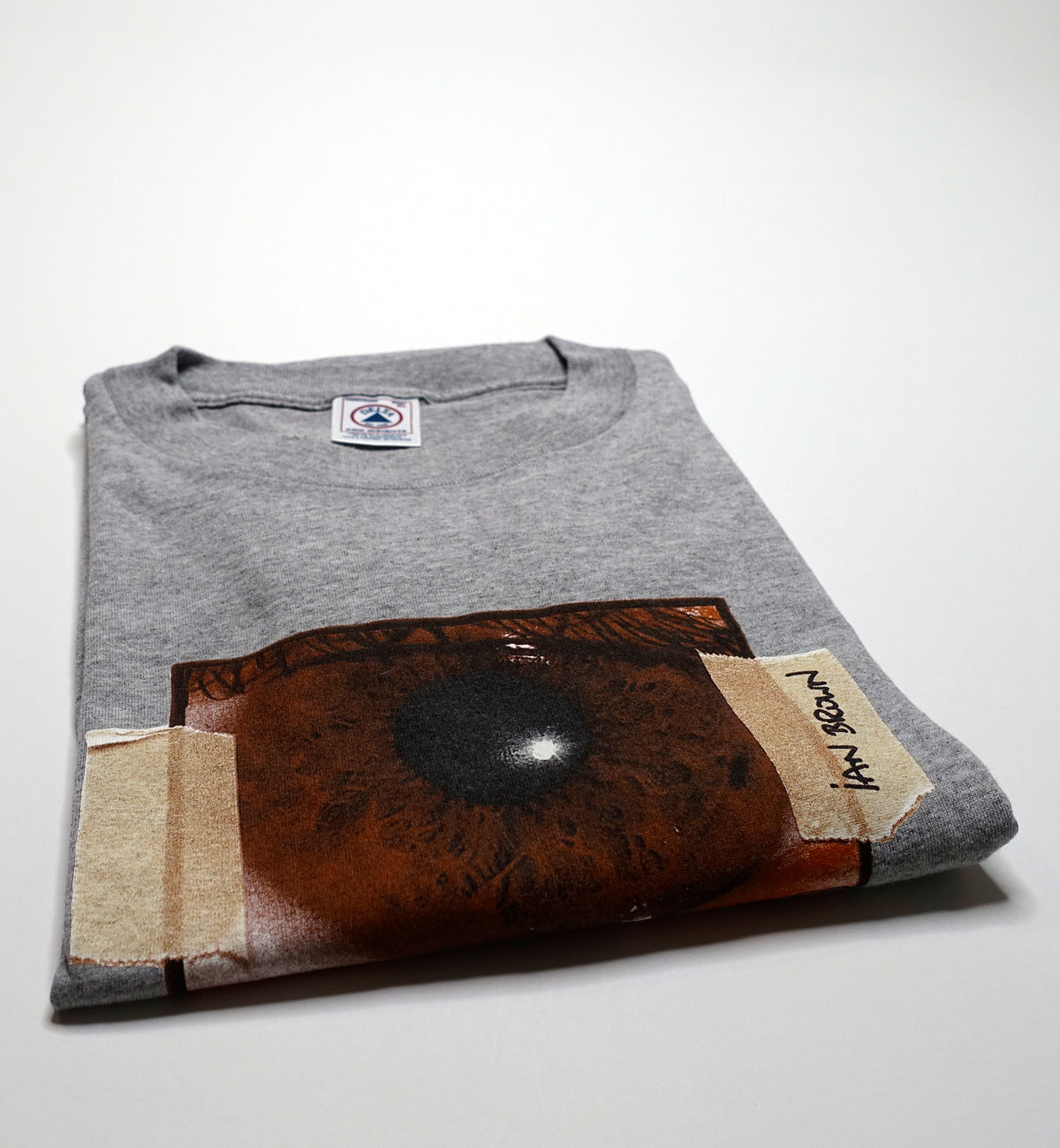 A gray t-shirt with a graphic design resembling an eye on the front, and a tag with 'Ian Brown' and 'Stone Roses' text on it.